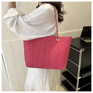 Detail of pink quilted nylon tote bag with golden metal chain strap worn by a model