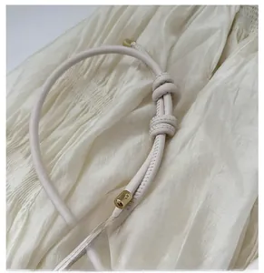 Detail of cream leather shoulder strap featuring a manual knot and gold metal tips