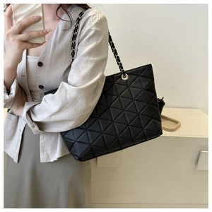 Close-up of black quilted tote bag with golden chain strap on a female model