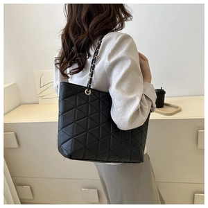Detail of black geometric quilted tote bag with gold chain strap on model shoulder