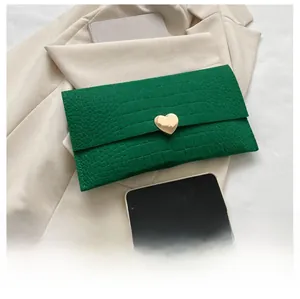 Detail of dark green crocodile texture envelope bag with gold heart-shaped magnetic clasp