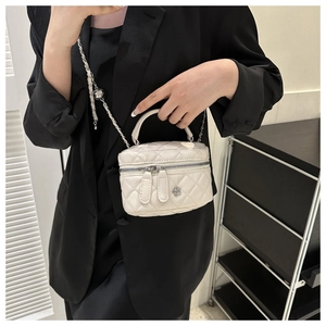 Sac boîte beige matelassé avec chaîne porté sur un blazer noir style élégant
