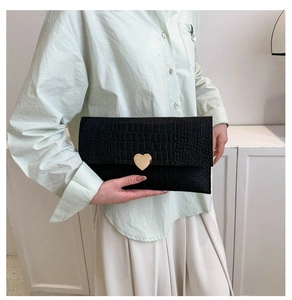 Close-up of black crocodile pattern envelope clutch with gold heart-shaped metal buckle