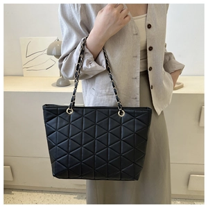 Detail of black geometric quilted tote bag with gold chain strap on model's shoulder