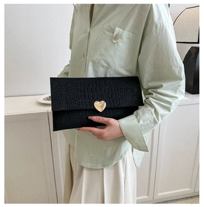 Chic black crocodile embossed envelope clutch with a gold heart clasp held by a model