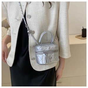 Détail du micro sac argenté matelassé avec fermoir fleur porté par un mannequin