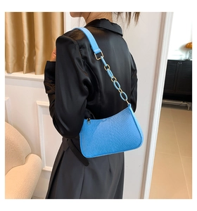 Detail of bright blue croc-effect shoulder bag with chain strap worn by a model