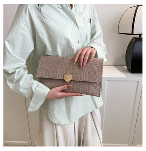 Taupe crocodile texture envelope clutch bag with a golden heart lock shown in hand
