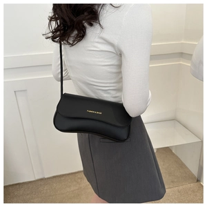 Side view of a chic black minimalist underarm bag with gold lettering on a white top