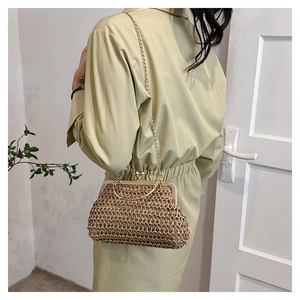 Détail d'un sac en paille tressée avec bandoulière chaîne dorée et fermoir en métal porté
