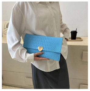 Detail view of light blue envelope clutch with crocodile texture and gold heart clasp