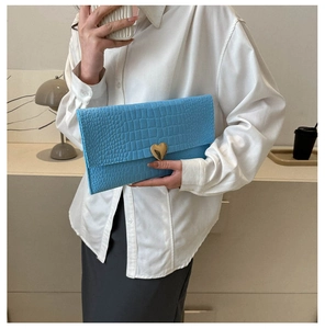 Macro detail of blue crocodile texture envelope clutch with a gold heart clasp