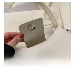 Detailed macro view of the round metallic magnetic closure on a cream leather shoulder bag