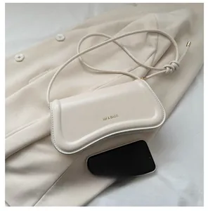 Detail der cremefarbenen Leder-Baguette-Tasche mit geknotetem Riemen und Handyvergleich