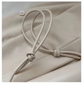 Detailaufnahme des beigen Taschengriffs mit Zierknoten und goldenen Metallkappen