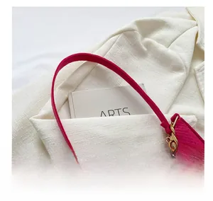 Close-up of fuchsia crocodile pattern leather bag with chunky gold chain on tweed fabric