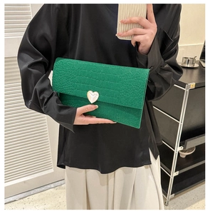 Detailed close-up of green crocodile pattern leather clutch with heart-shaped buckle