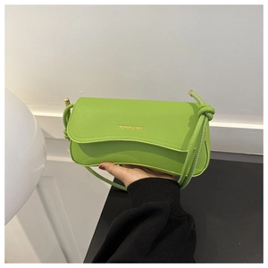 Detail of neon green leather crossbody bag with gold fashion lettering and knotted strap