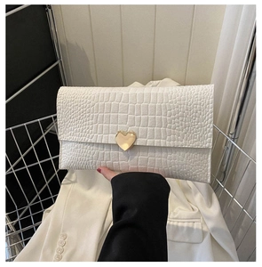 Detailed view of crocodile pattern leather on a white clutch with a gold heart buckle
