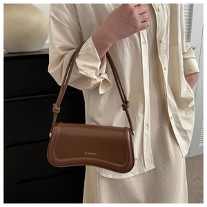 Nahaufnahme der braunen glänzenden Ledertasche mit Goldlogo und geknotetem Riemendetail