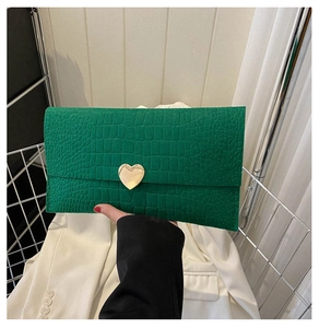 Detail of dark green crocodile texture envelope clutch with a gold heart lock buckle