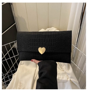 Detail of black crocodile texture envelope clutch with gold heart-shaped metal buckle