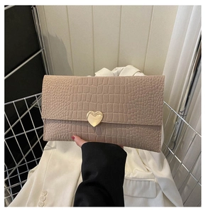 Detail of beige faux crocodile envelope clutch featuring a gold heart magnetic clasp