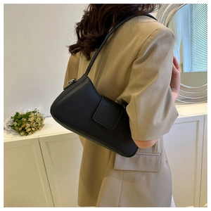Close-up of minimalist black faux leather shoulder bag worn by model in chic interior