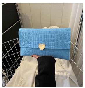 Detail of light blue crocodile embossed clutch bag with a golden heart-shaped clasp