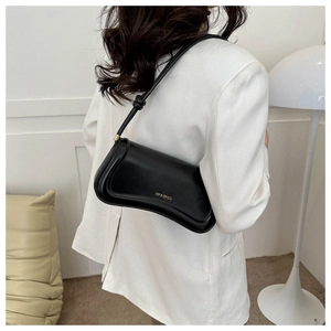 Detail einer schwarzen Halbmond-Schultertasche mit goldenem Logo am Model im weißen Blazer
