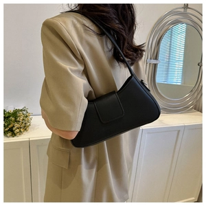 Minimalist black matte leather baguette bag worn by a model in a stylish home setting