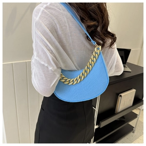 Detail of sky blue crescent underarm bag with gold chain strap shown on model's shoulder