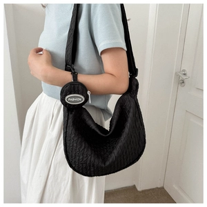 Detail view of black pleated crescent bag featuring a detachable round mini coin purse pouch