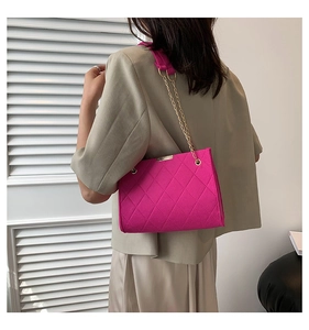 Detail of bright pink felt shoulder bag with quilted diamond pattern and gold chain strap