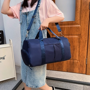 Deep blue nylon cylinder travel duffel bag with gold hardware shown on a model