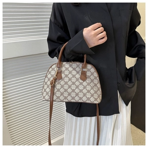Detail of a beige and brown patterned shell bag with brown leather strap and gold buckle