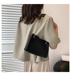 Chic quilted black felt chain bag worn over a light green blazer against white walls