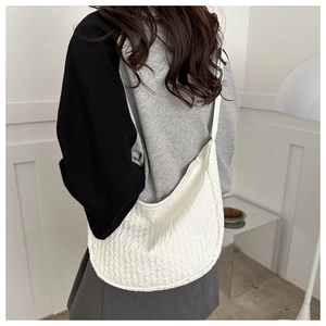 Side view of white pleated crescent bag showing the rich textured fabric and shoulder strap