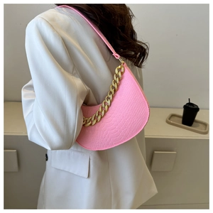 Pink croc-embossed crescent bag with gold chain strap worn over a white blazer