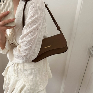 Brown leather underarm bag with gold lettering and slim shoulder strap on white dress