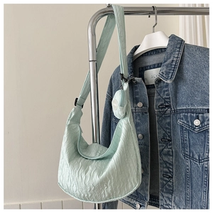 Detail of light green quilted crescent bag featuring wide strap and mini coin purse accessory