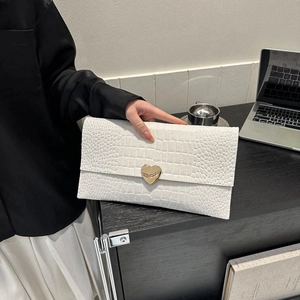 White crocodile pattern envelope clutch bag with gold heart clasp held by a woman