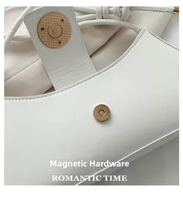 Detail of golden magnetic closure on a minimalist white matte leather shoulder bag