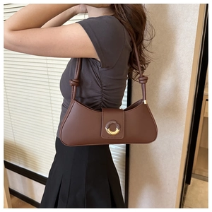 Brown underarm bag with knot strap detail and round metal clasp worn by a model