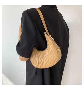 Detail of khaki hobo bag with pleated texture worn over a black blazer by a model