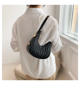 Detail view of black Matelassé crescent bag with gold hardware worn on shoulder
