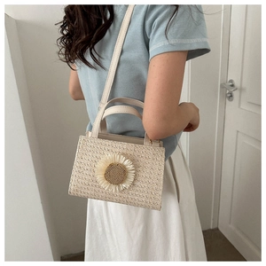 Detail of straw woven crossbody bag featuring a large sunflower ornament and top handle