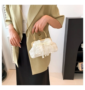Detail van witte tweed handtas met gouden handvat en mesh strik met parelversieringen