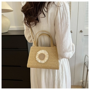 Detail of a beige straw crossbody bag with white daisy decor in a lifestyle setting