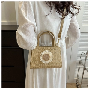 Detail of hand-woven straw bag with a white daisy floral applique and leather handle